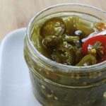 Small open jar of candied jalapenos with a fork in the jar.