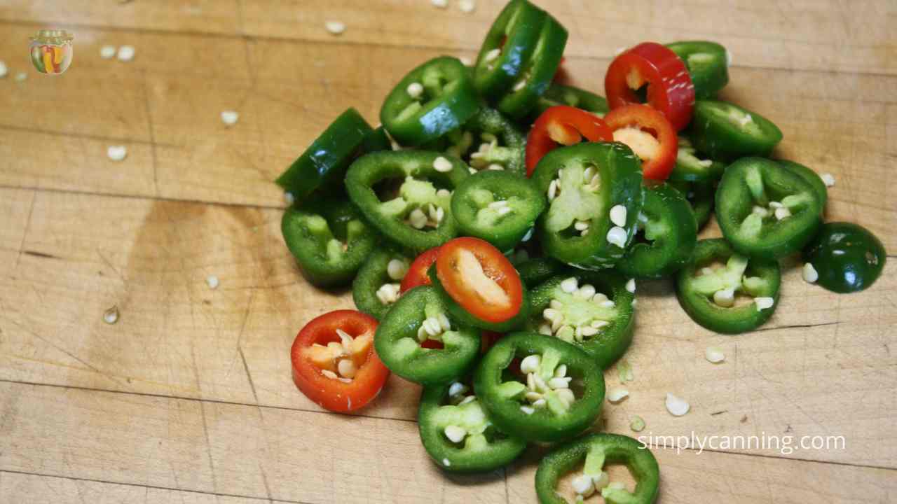 Handful of green and red jalapeno peppers sliced into rounds, piled on a wood counter. 