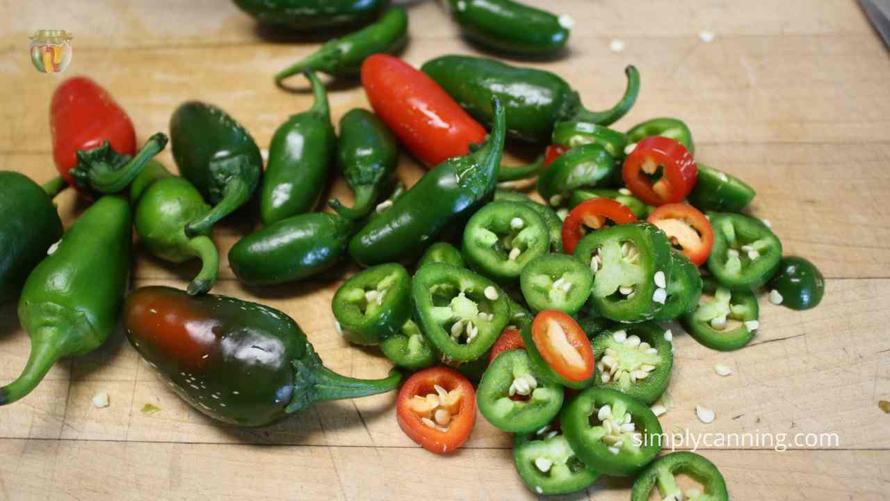 – Stack of red and green jalapenos some chopped into rounds sitting on a wood counter. 