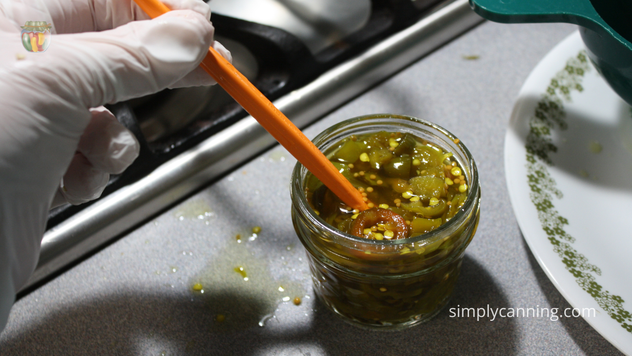 De-bubbling small jar of hot peppers, white goved hand working with an orange peeler.