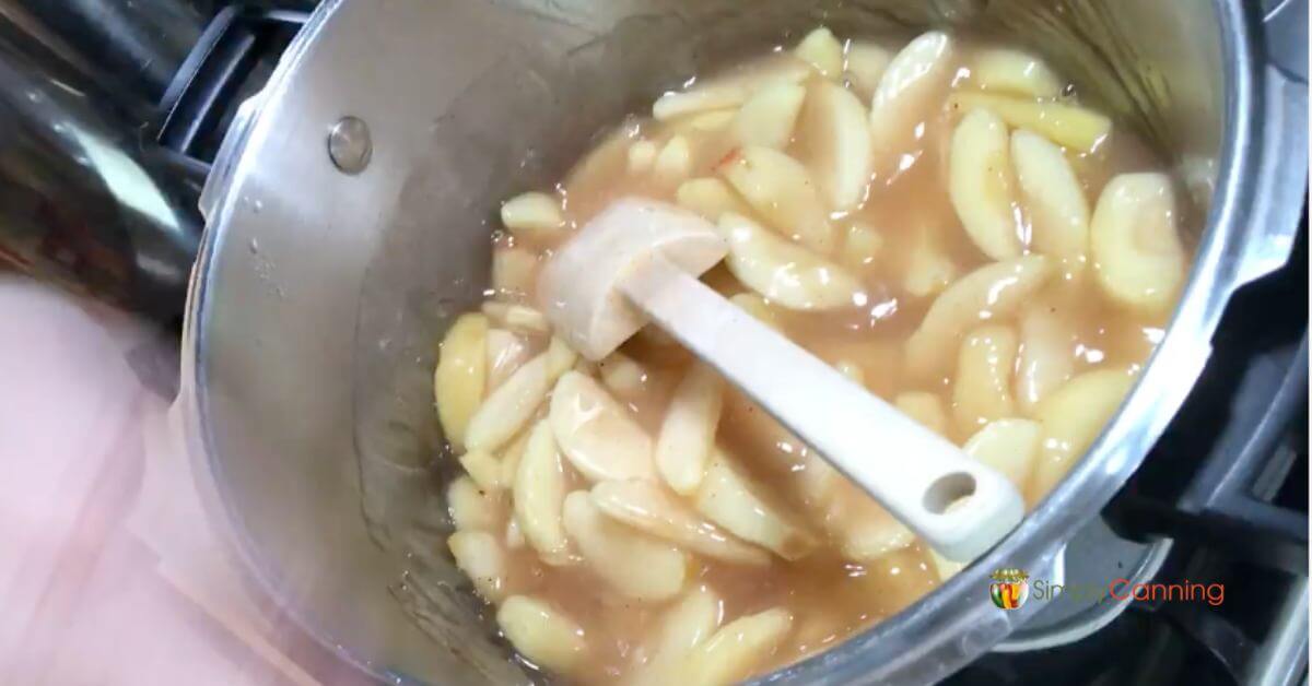 Cooking apple pie filling in a pot, stirring with a rubber spatula.