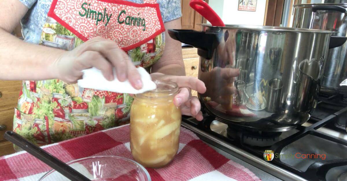 Sharon at her counter wiping the rim of a pint jar of pie filling.