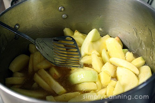 Stirring together apple slices and syrup in a large pot.