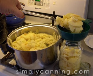 Spooning hot apple slices into a canning jar through a canning funnel.