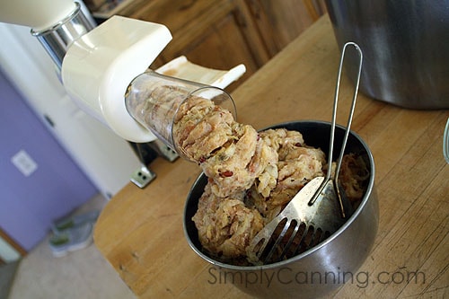 Apple pulp being pushed out of the food mill into a bowl.