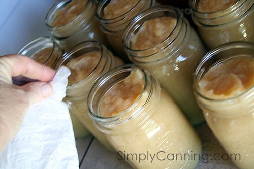 Wiping rims of the jars of applesauce with a wet paper towel.