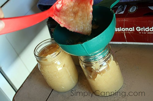 Pouring applesauce into canning jars through a canning funnel.