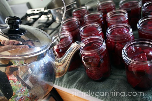 Pouring water from tea kettle into jars packed with beets.