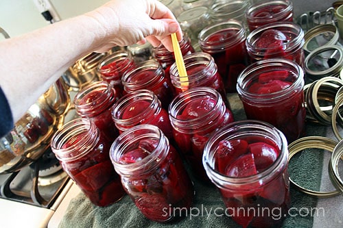 Removing bubbles from jars packed with deep red beet pieces.