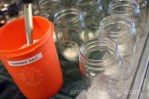 Measuring canning salt from the orange canister into each empty canning jar.