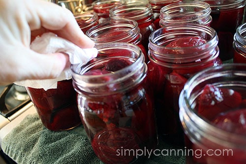 Wiping rim of a jar of beets with a wet paper towel.