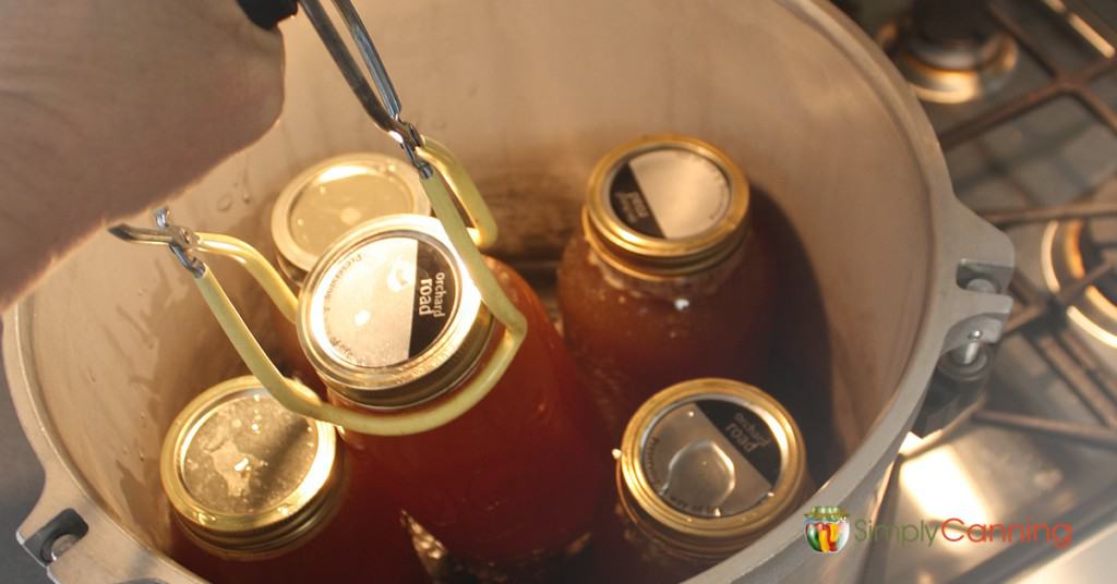 Putting full jars of broth into the pressure canner using a jar lifter.