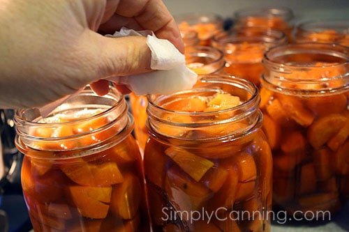 Wiping rims of jars packed with orange carrot pieces.