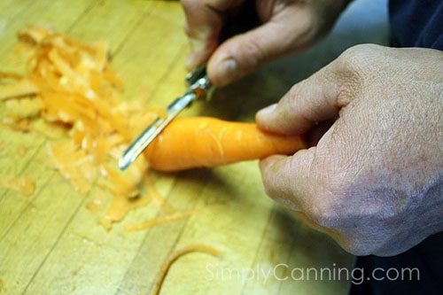 Peeling a carrot by hand using a small metal vegetable peeler.