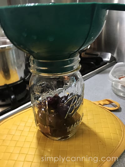 Packing a clear jar with pitted cherries.