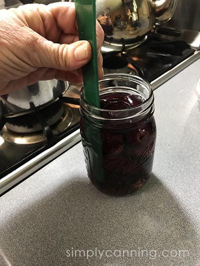 Removing bubbles and measuring headspace in a jar of cherries.