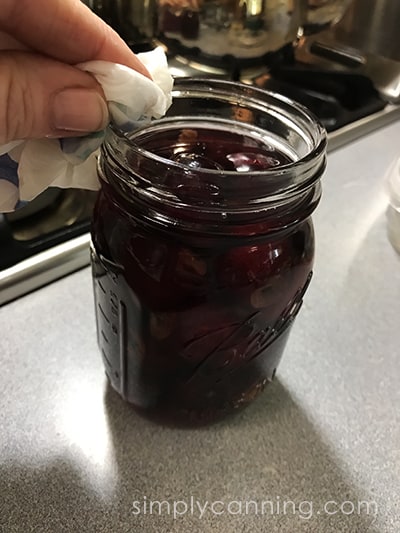 Wiping the rim of the jar of cherries with a wet paper towel.