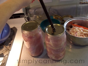 Placing flat lids on jars packed with raw chicken.