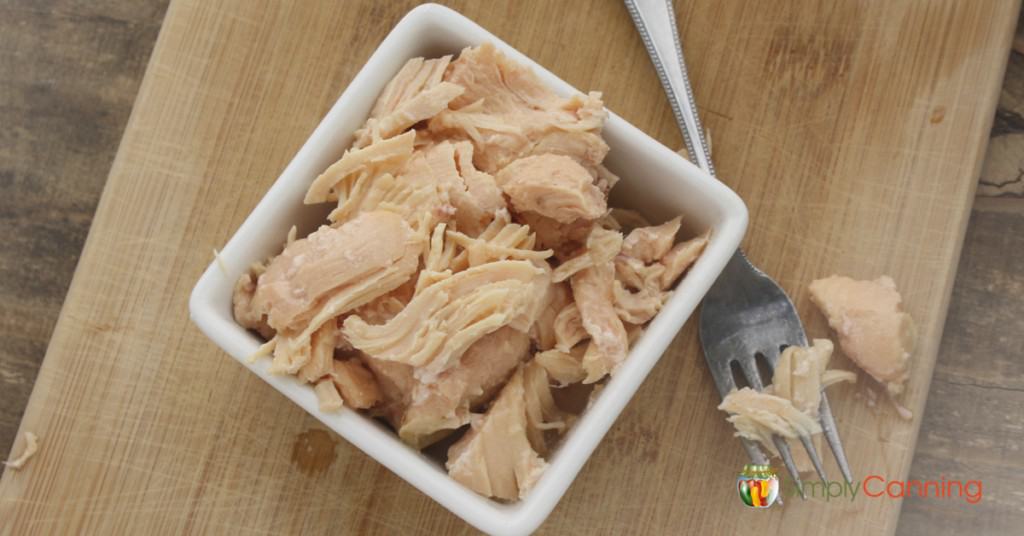 Shredded cooked chicken in a square dish with a fork sitting beside it.