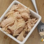 Shredded cooked chicken in a square dish with a fork sitting beside it.