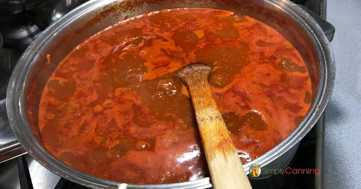 Pot of chili simmering on the stove with a wooden spoon to stir and prevent sticking.