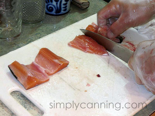 Cutting bright fish into smaller pieces on a white cutting board.