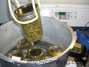 Lifting a pint jar of processed green beans out of the steaming hot canner.