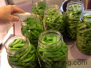 Wiping the rims of the green bean jars with a wet paper towel.