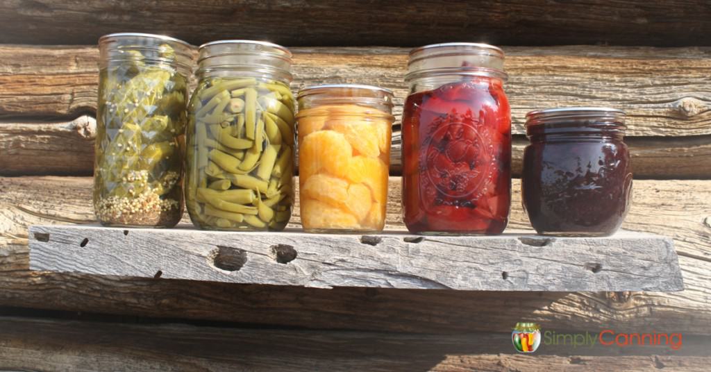 A variety of canning jars sitting in a row with the sun shining on them.