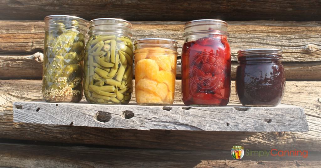 A variety of canning jars sitting in a row with the sun shining on them.