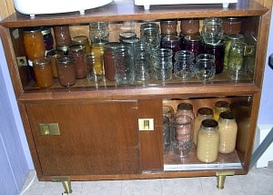 Filled and empty canning jars in the vintage cabinet with the sliding door in the front.