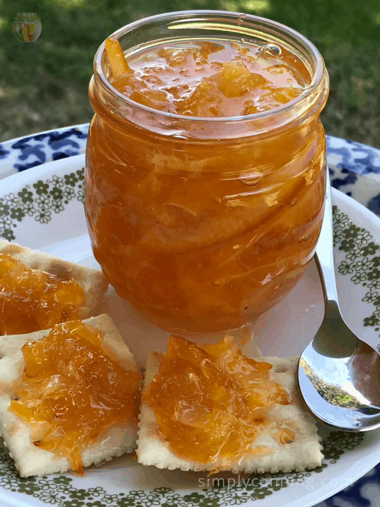 Crackers spread with orange marmalade sitting next to an open jar of orange marmalade.