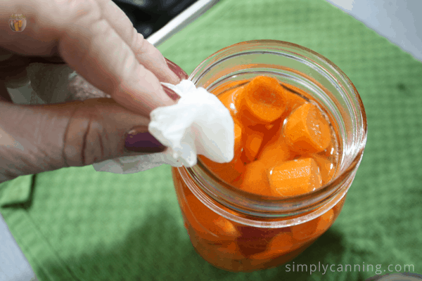 Wiping the rim of a jar of carrots.