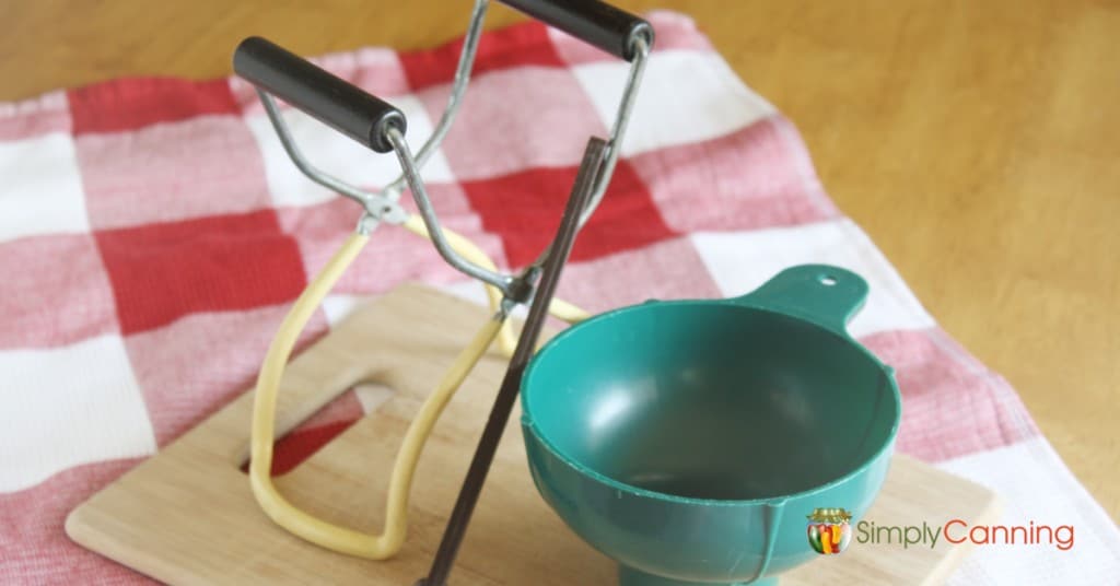 Various canning tools sitting on a wooden cutting board in the kitchen.