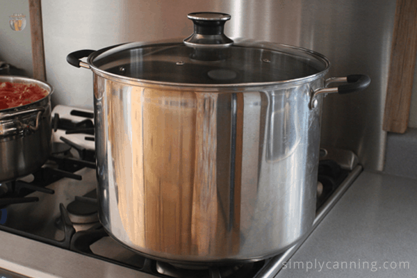 Stainless steel water bath canning with a glass lid sitting on the stovetop.