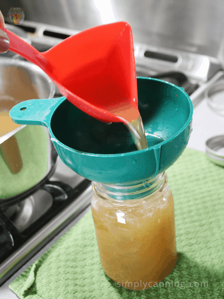 Pouring broth through a canning funnel into a pint jar.