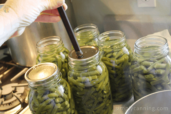 Placing lids with the magnetic lid lifter onto jars packed with green beans.