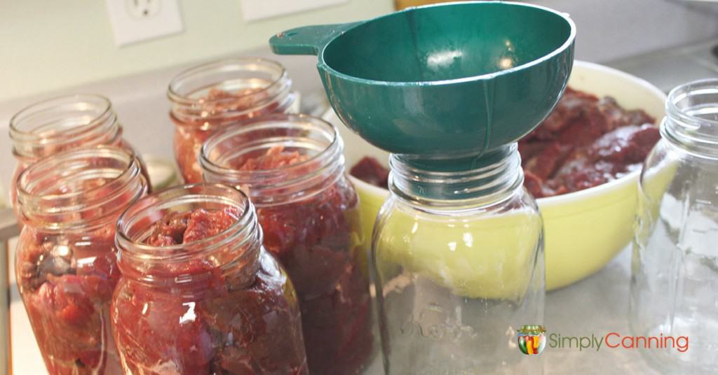 Packing quart jars with pieces of raw meat.