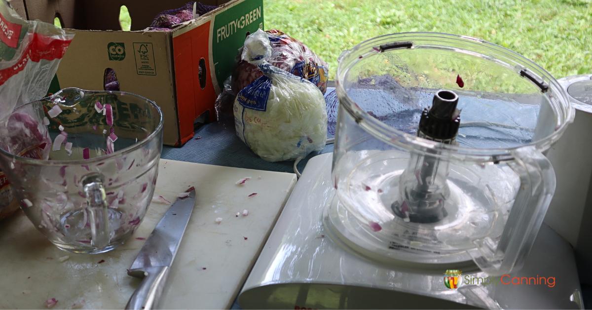 Outdoor table with food chopper, clear bowl, chopped onion scattered about, messy efficiency!