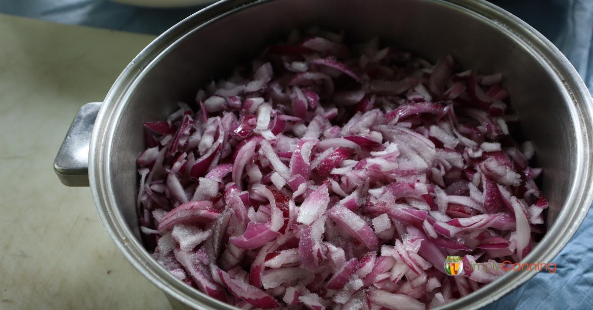 Large pot with chopped red onions sprinkled with salt.