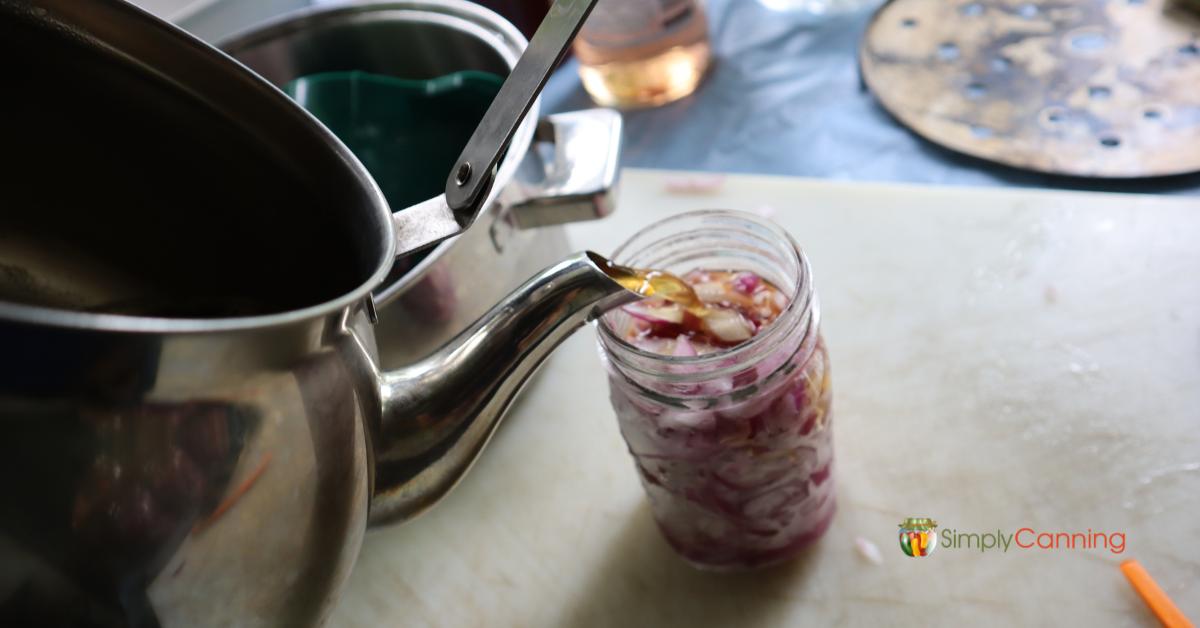 Filling a pint jar of choppped onions with honey and wine sauce from a tea kettle.