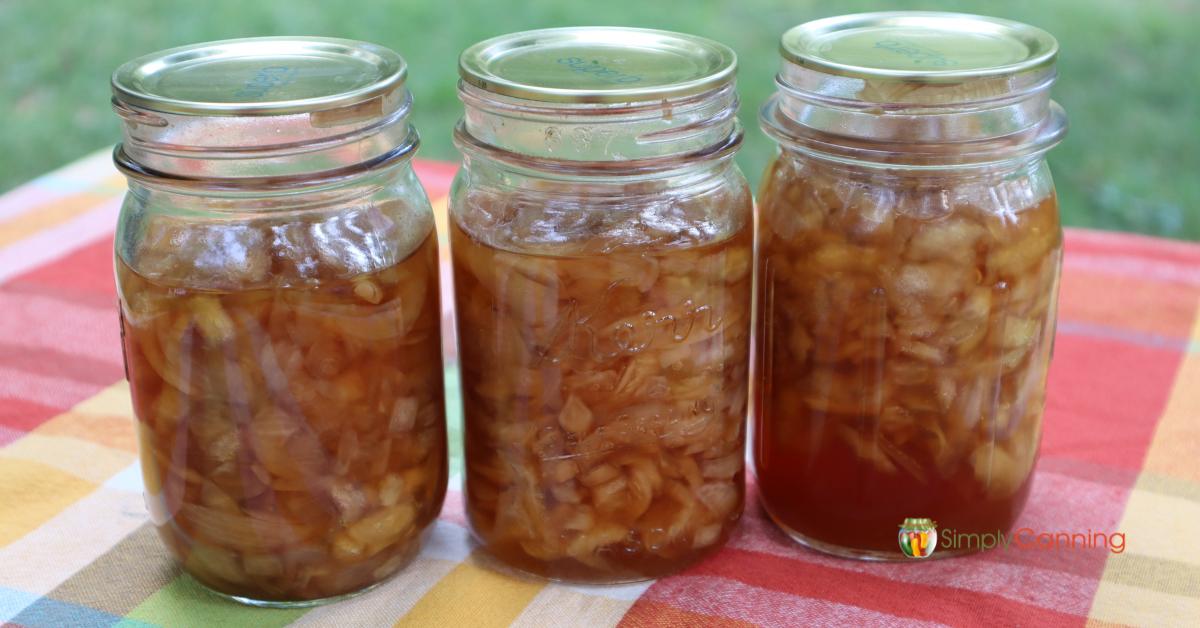 3 pint jars of home canned onions in honey sauce on an autumn colored tablecloth.