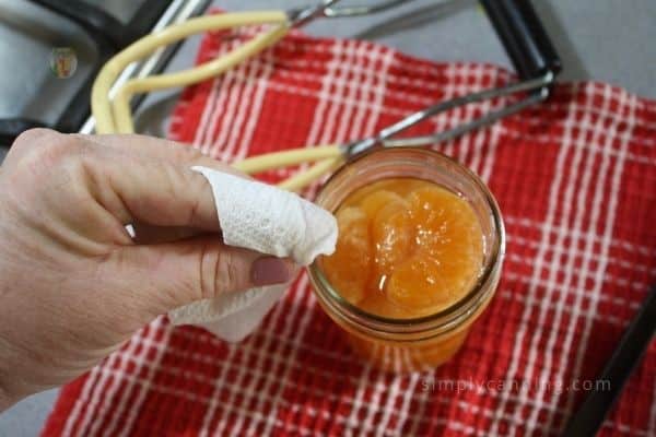 Wiping the rim of a jar of oranges with a wet paper towel.