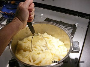 Mashing up pears in a pot with a potato masher.