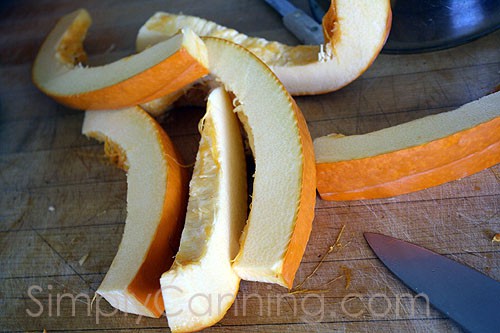 Slicing pale colored pumpkin into smaller pieces with skin still attached.