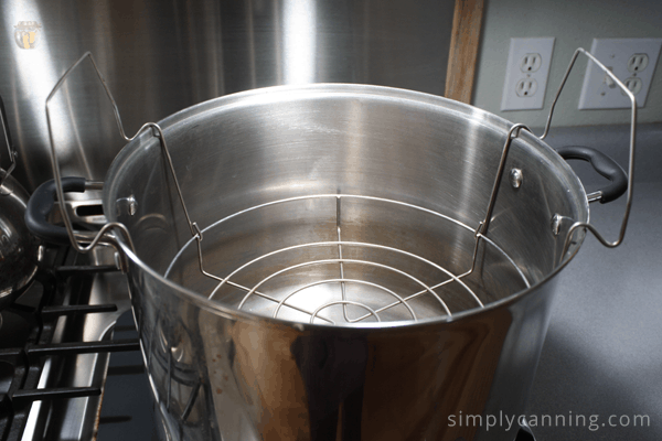 A canning rack plunged into water in a pot.