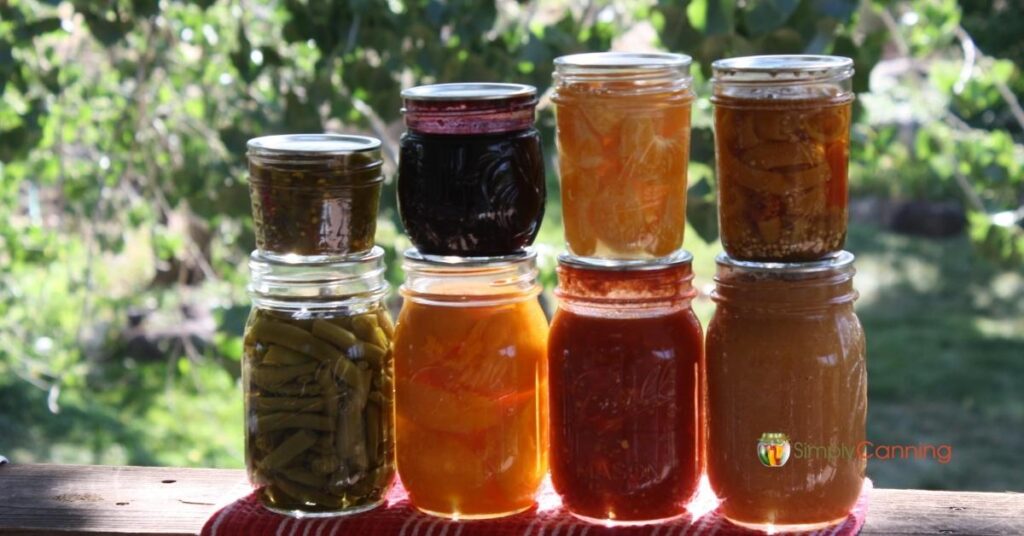 Eight Canning Jars on a deck railing with the sun shining lighting up the jars from the back.