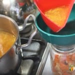 Pouring soup into a canning jar through a canning funnel with the pot of soup to the side.