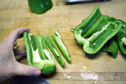 Chopping half of a green bell pepper into strips.