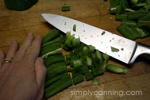 Chopping strips of green pepper into pieces using a large chef's knife.